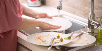 Young woman doing the dishwashing: washing a white plate under r